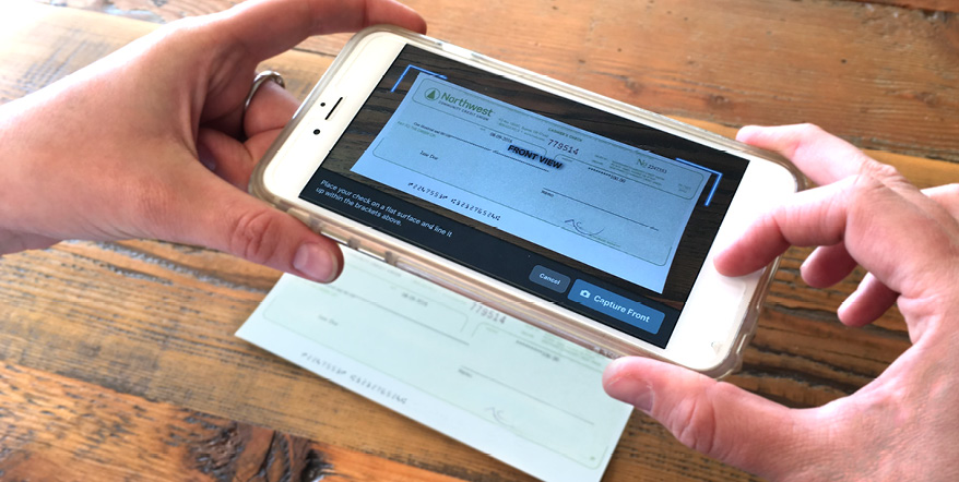Hands holding a smartphone and taking a picture of a check for uploading.