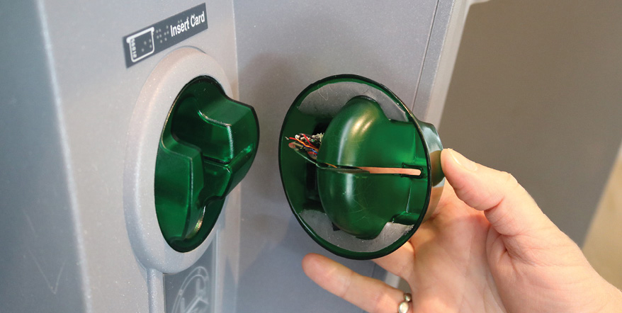 Image of a person using a mirror to spot a card skimmer in an ATM