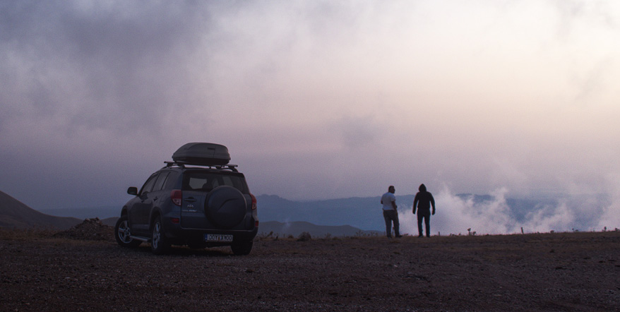 Image of two people overlooking a cliff next to their parked car.