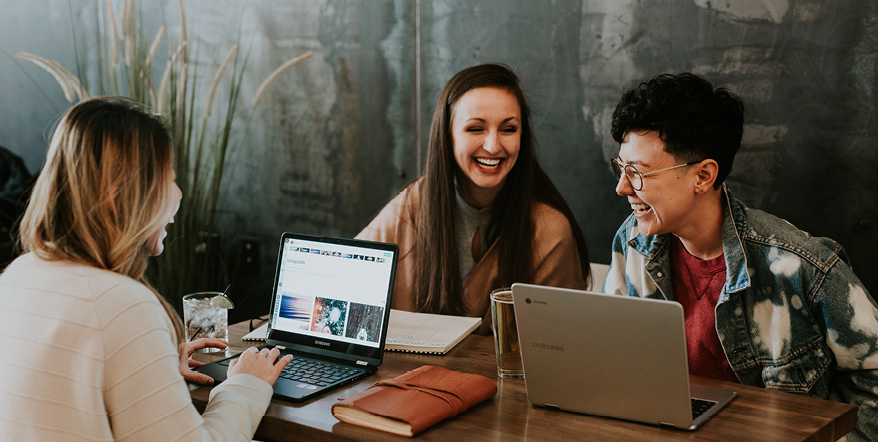 Image of three college students laughing together while working on their laptops.